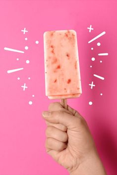 a hand holding up a popsicle on a pink background