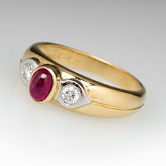 This lovely ring is centered with one (1) oval cabochon cut natural ruby set into a bezel. The shoulders are each accented with one (1), flush set, round brilliant cut diamond. The ring measures 6.7mm at the top, rises 6.8mm above the finger, tapering to 3.1mm wide and 0.8mm thick at the base of the shank. This ring is currently a size 8.5. Luxury Ruby And Diamond Oval Cabochon Ring, Luxury Ruby Ring With Oval Cabochon Diamond, Formal Ruby Three Stone Ring With Diamonds, Classic Diamond Ring With Cabochon Cut, Classic Diamond Cabochon Ring, Oval Cabochon Ruby Ring With Diamonds, Formal Ruby Ring With Diamond And Oval Cabochon Shape, Formal Oval Cabochon Ruby Ring With Diamond, Luxury Oval Three-stone Ruby Ring