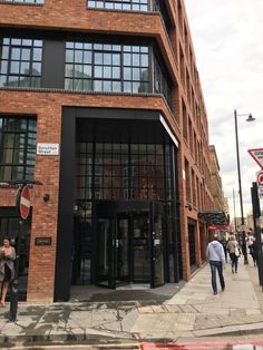 two people walking down the sidewalk in front of a brick building with glass doors and windows