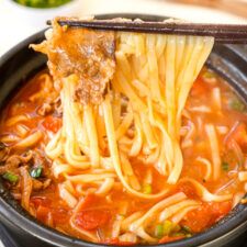 a close up of a bowl of soup with noodles and meat being held by chopsticks