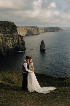 a bride and groom standing on the cliff overlooking the ocean