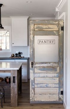 an old door is opened to reveal a kitchen with white cabinets and wood floors, along with a bar stools