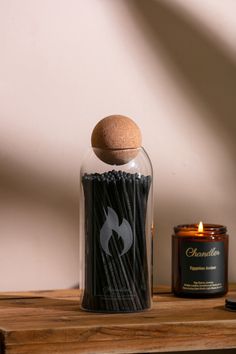 a candle and some matches in a glass jar on a wooden table next to it