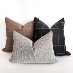 three different colored pillows sitting on top of each other in front of a white wall