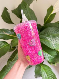 a hand holding a pink glitter cup with hearts on the lid and straw in it