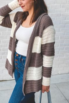 a woman is walking down the street with her hand on her head and wearing a striped cardigan