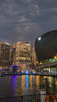 the city skyline is lit up at night with lights reflecting on the water and buildings in the background