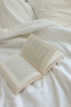 an open book sitting on top of a bed next to white sheets and pillow covers