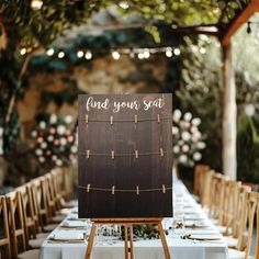 a sign that says find your seat sitting on top of a wooden easel with string lights strung from the ceiling