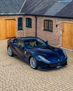 a blue sports car parked in front of a brick building with wooden doors and windows