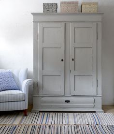 a white armoire sitting next to a blue chair in a living room on top of a rug