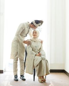 a man and woman kissing while sitting on a chair in front of a large window