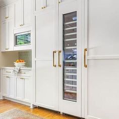 a kitchen with white cabinets and wood flooring next to a window that has glass doors