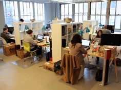 people working at desks in an office with large windows and lots of bookshelves