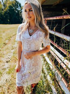 a beautiful blonde woman wearing a tiara standing in front of an old rusty fence