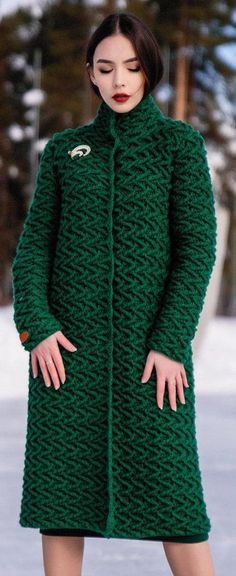 a woman in a green coat standing on snow covered ground with her hands behind her back