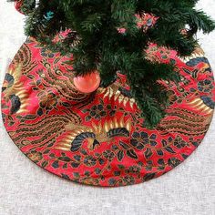 a small christmas tree in a red vase on a round placemat with gold and black designs