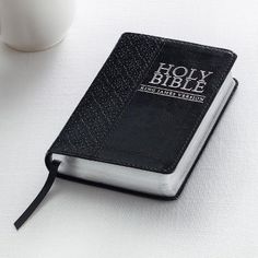 a black bible sitting on top of a white table next to a cup of coffee