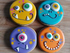 four decorated cookies with eyes and mouths on top of a wooden table next to each other