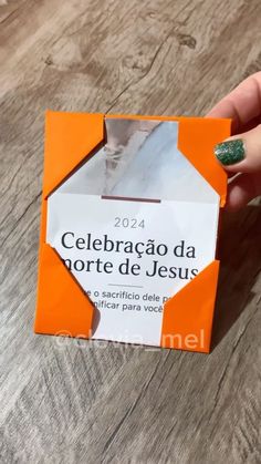 a person holding up a small orange and white origami box with the words celebracao da morte de jesus on it