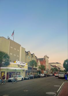 cars are parked on the street in front of buildings and palm trees, with an american flag flying above them