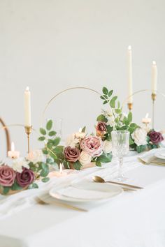 the table is set with white and pink flowers, greenery and gold place settings