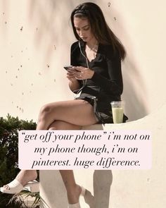 a woman sitting on top of a white wall next to a cup and cell phone