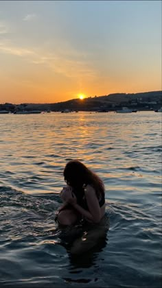 a woman is sitting in the water with her cell phone to her ear as the sun sets