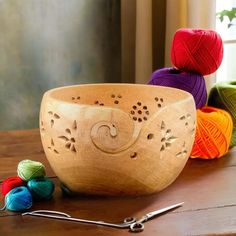 a wooden bowl sitting on top of a table next to crochet hooks and balls of yarn