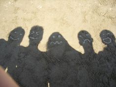 four people with faces drawn on their feet standing in the sand and looking up at something