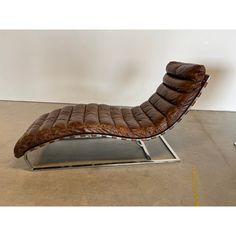 a brown leather chaise lounge chair sitting on top of a metal frame in a room