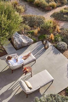 a woman laying in a chair on top of a patio next to some trees and bushes