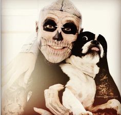 a man in skeleton makeup holding a small dog with his face painted white and black