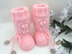 a pair of pink knitted boots sitting on top of a white table next to flowers