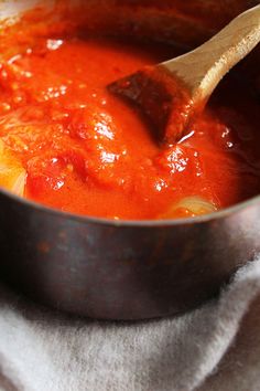 a wooden spoon in a metal pot filled with tomato sauce on top of a white towel