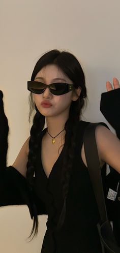 a woman with long black hair wearing sunglasses and holding her hands up in the air