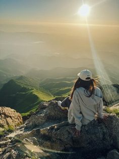 a woman sitting on top of a large rock in the middle of a mountain range