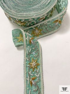 a green ribbon with gold stars and beads on the edge is laying on a white surface