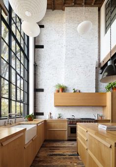 an industrial style kitchen with wooden cabinets and white brick walls, along with black framed windows