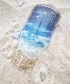 a glass bottle sitting on top of a sandy beach next to sea shells and sand