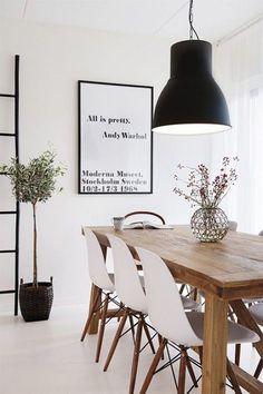 a dining room table with white chairs and a black lamp hanging from the ceiling over it