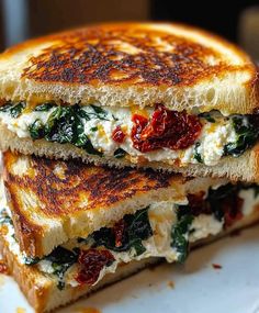 two grilled cheese sandwiches stacked on top of each other with spinach and sun dried tomatoes