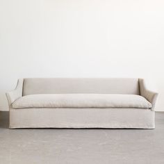 a white couch sitting on top of a cement floor next to a wall with a plant in it