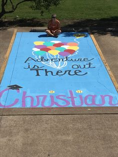 a person sitting on the ground in front of a blue sign that says adventure is out there