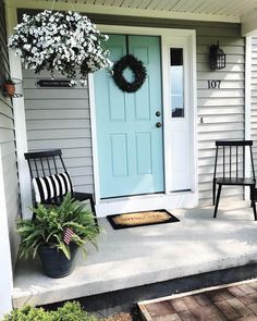 two chairs are sitting on the front porch with a wreath hanging above them and a potted plant next to it