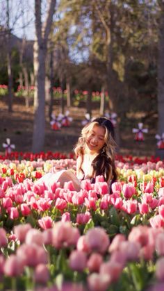 a woman sitting in the middle of a field full of pink and yellow tulips