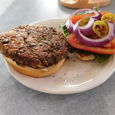 a hamburger with lettuce, tomato and onion on it sitting on a plate