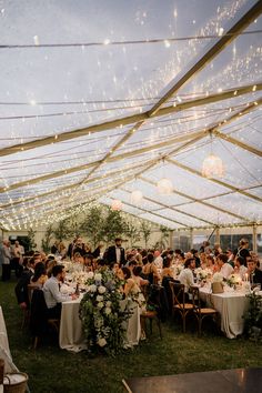 a large group of people sitting at tables under a tent with lights on the ceiling