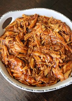 a white bowl filled with shredded meat on top of a wooden table next to a fork