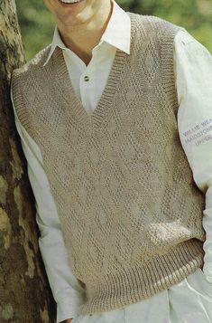 a man wearing a sweater vest leaning against a tree